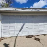 White garage door with weeds nearby.