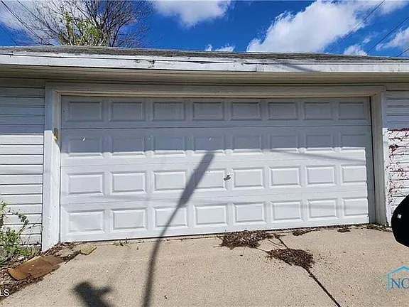 White garage door with weeds nearby.
